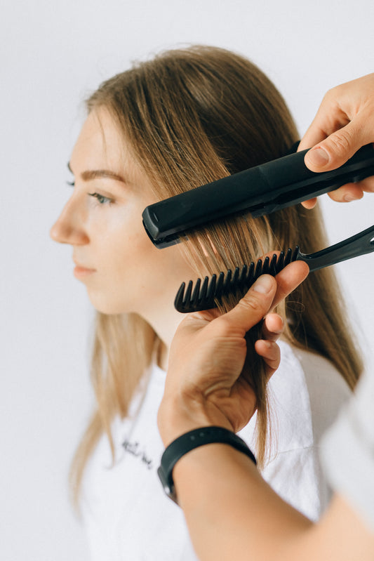 Hairstylist realizza un liscio perfetto con una piastra professionale su capelli lunghi, lisci e luminosi in un salone di acconciatura.